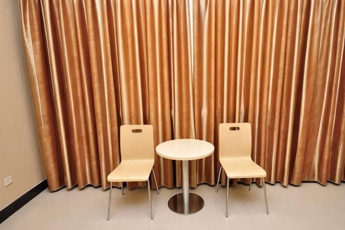 Une pièce avec deux chaises et une table, un fond constitué d’un rideau et un mur uni.