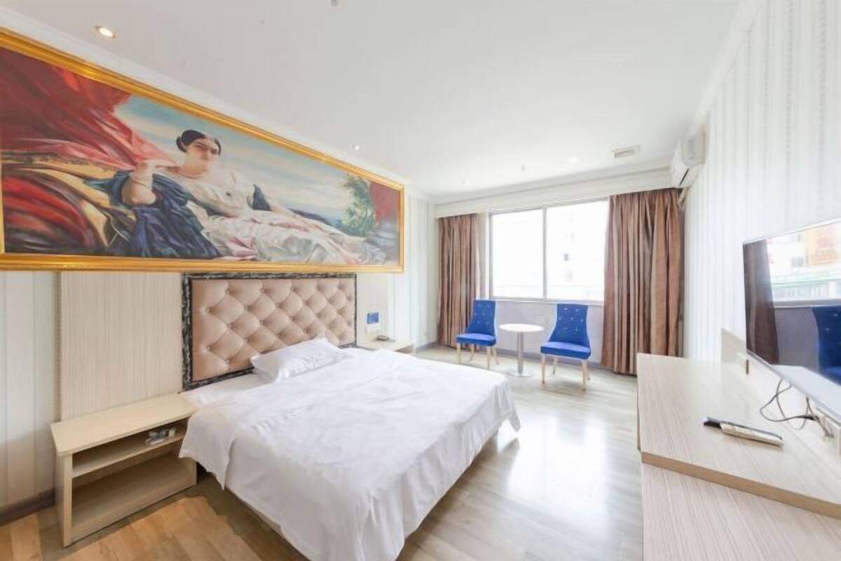 Une chambre d’hôtel avec un grand lit, une télévision, un bureau et un tableau au mur.