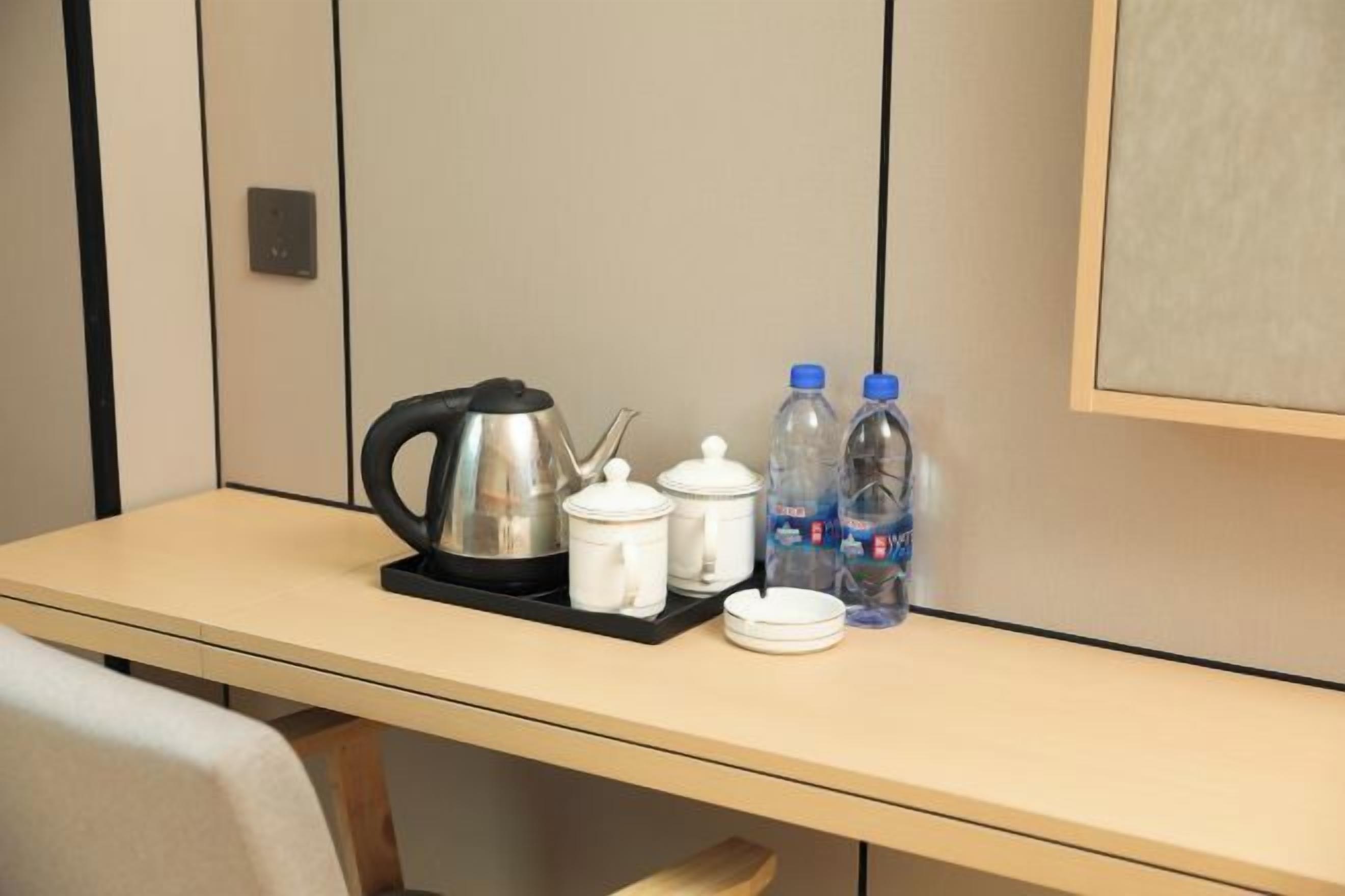 Une chambre d’hôtel avec une table sur laquelle sont disposés une bouilloire, des théières, des tasses et des bouteilles d’eau.