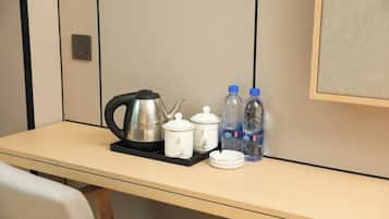 Een hotelkamer met een tafel, compleet met waterkoker, theepotten, kopjes en flessenwater.