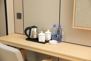 Una habitación de hotel con una mesa dispuesta con una tetera, teteras, tazas y agua embotellada.
