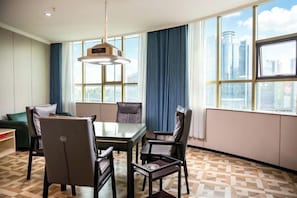 Une chambre d’hôtel équipée d’une table à manger, de chaises, d’un canapé et de grandes fenêtres donnant sur la ville.