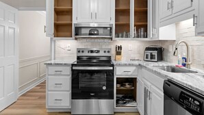 A modern kitchen with white cabinetry, a stainless steel oven, a microwave, and a dishwasher.