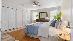 A bedroom with a bed, bedside table, lamp, dresser, mirror, and ceiling fan.