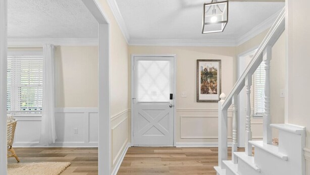 A hallway with a wooden floor, a white door, and a staircase with white railings.