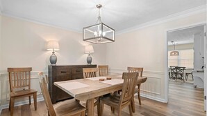 A dining area with a wooden table and chairs, a chandelier, and two wall-mounted lamps.