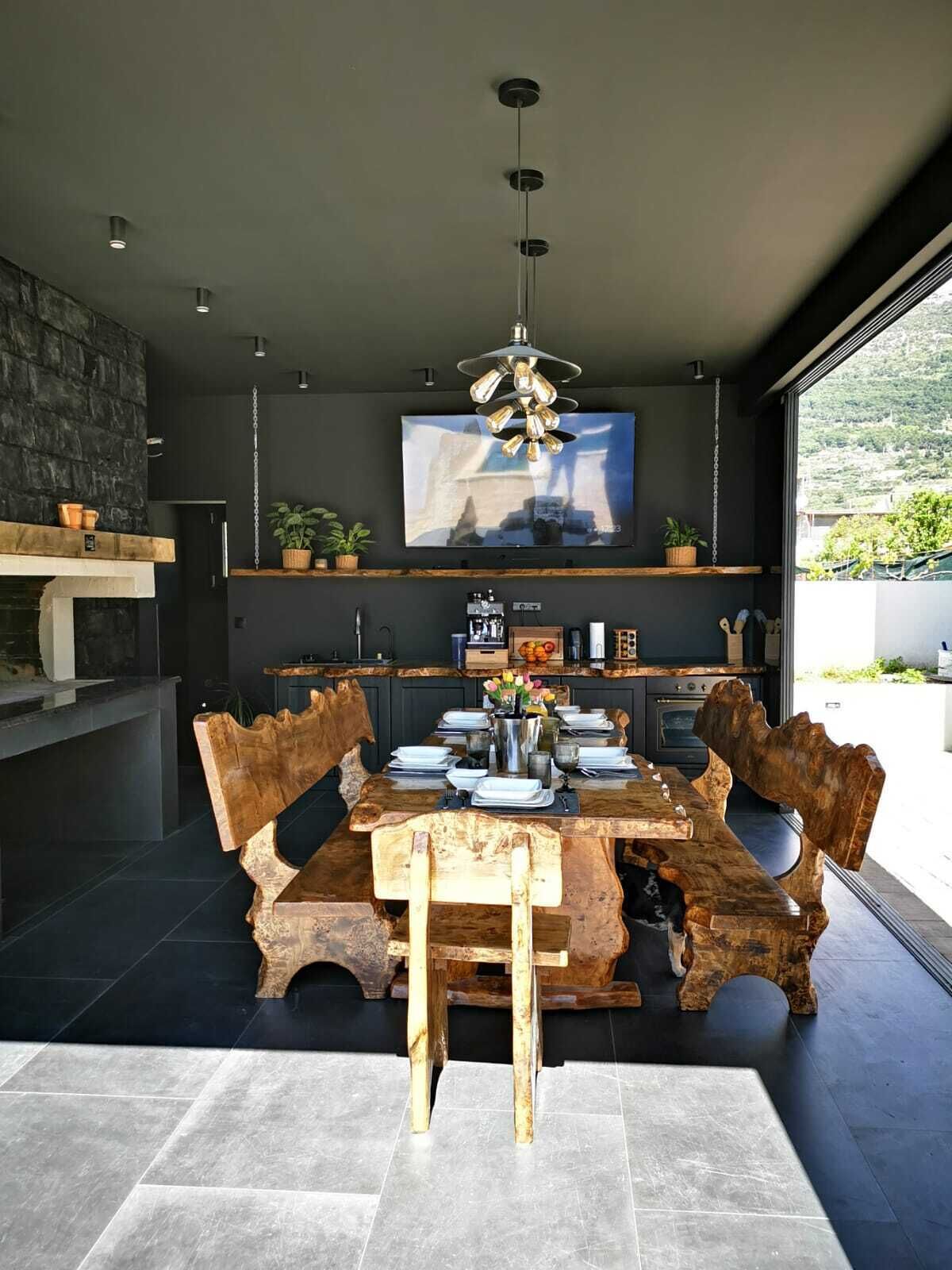 Zona pranzo moderna con un grande tavolo di legno e panche, una televisione a parete e vista sull'esterno.