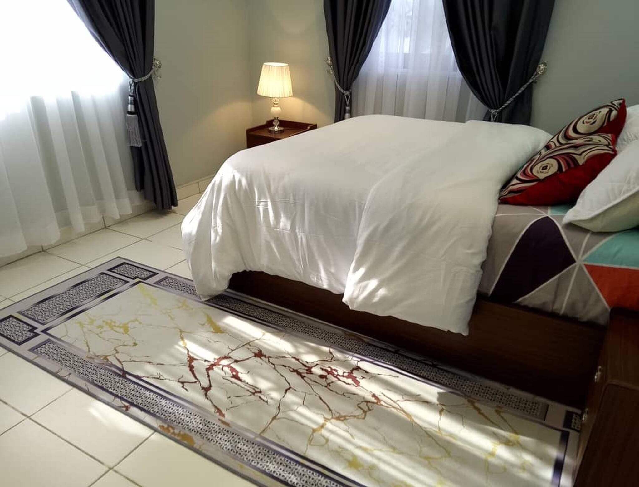 Una camera da letto con un letto, un comodino con una lampada e un tappeto decorativo.