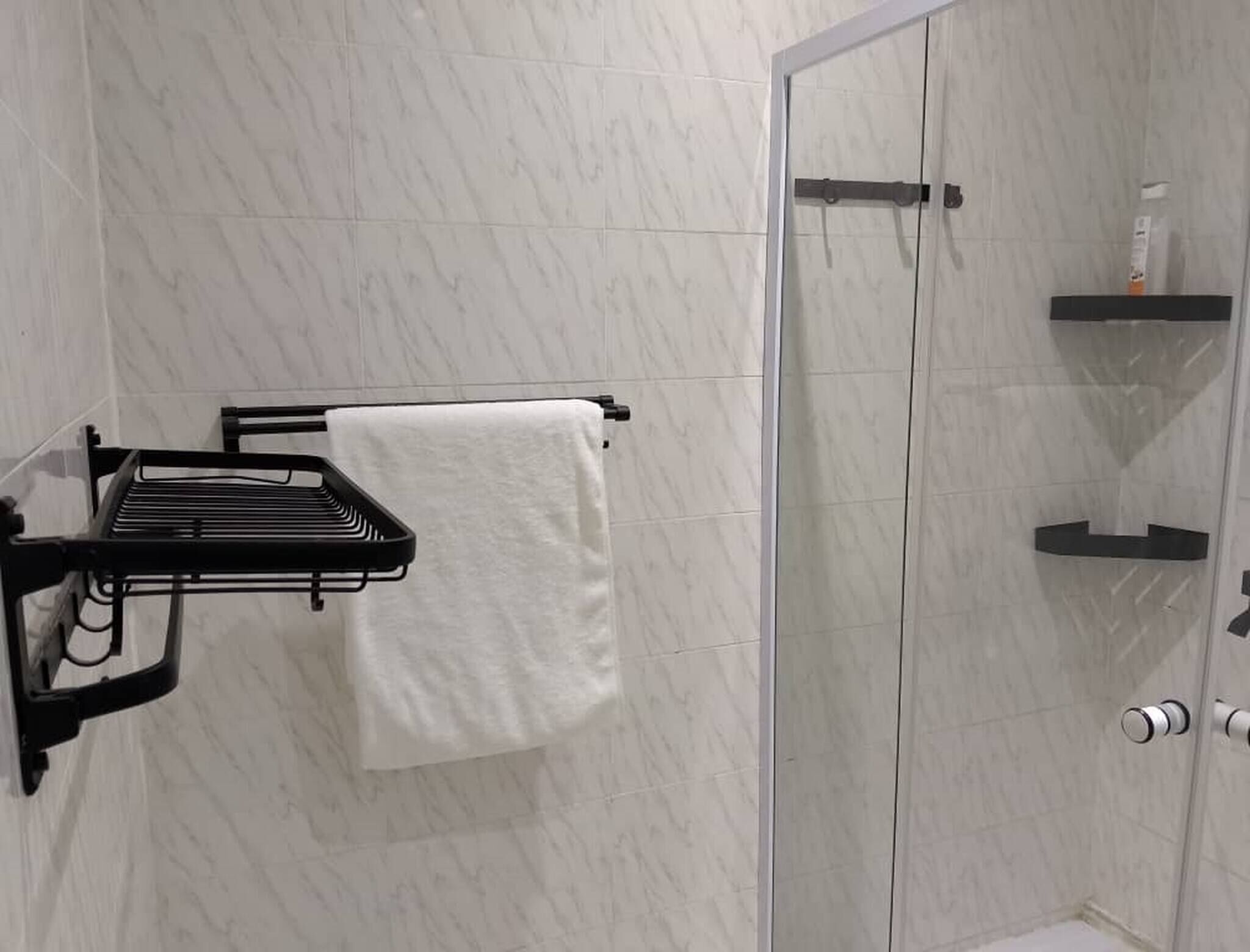 A bathroom with a shower, a towel rack, and a soap dispenser on a shelf.