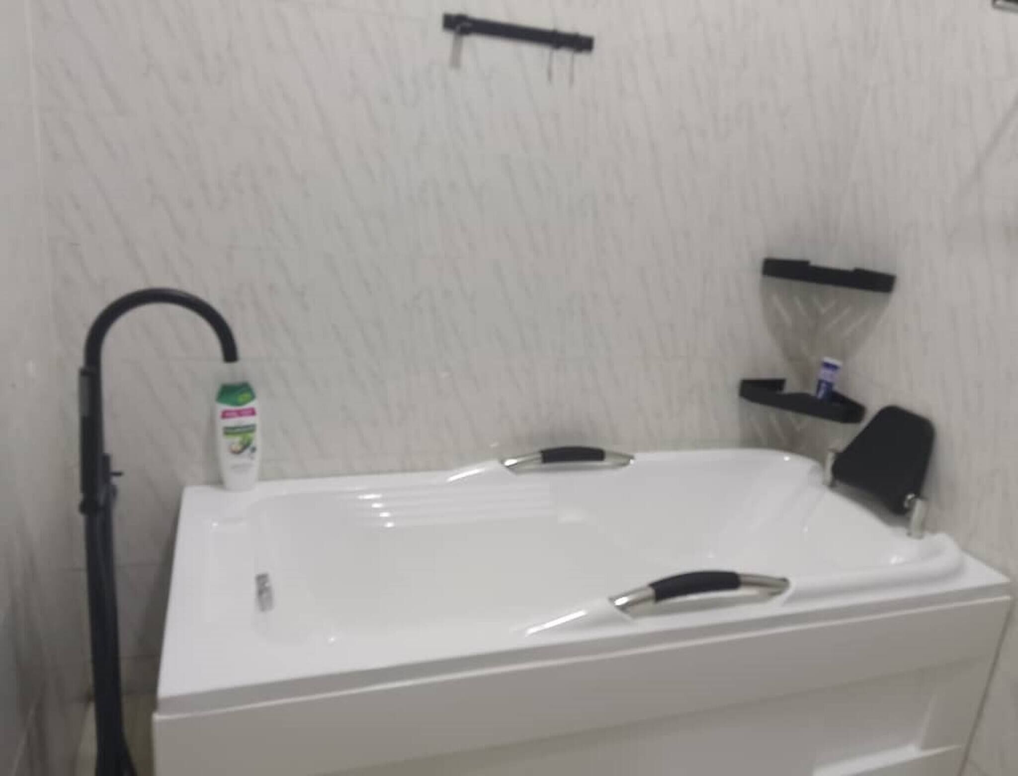 Une baignoire blanche avec un robinet noir et une bouteille de shampoing posée sur le bord.