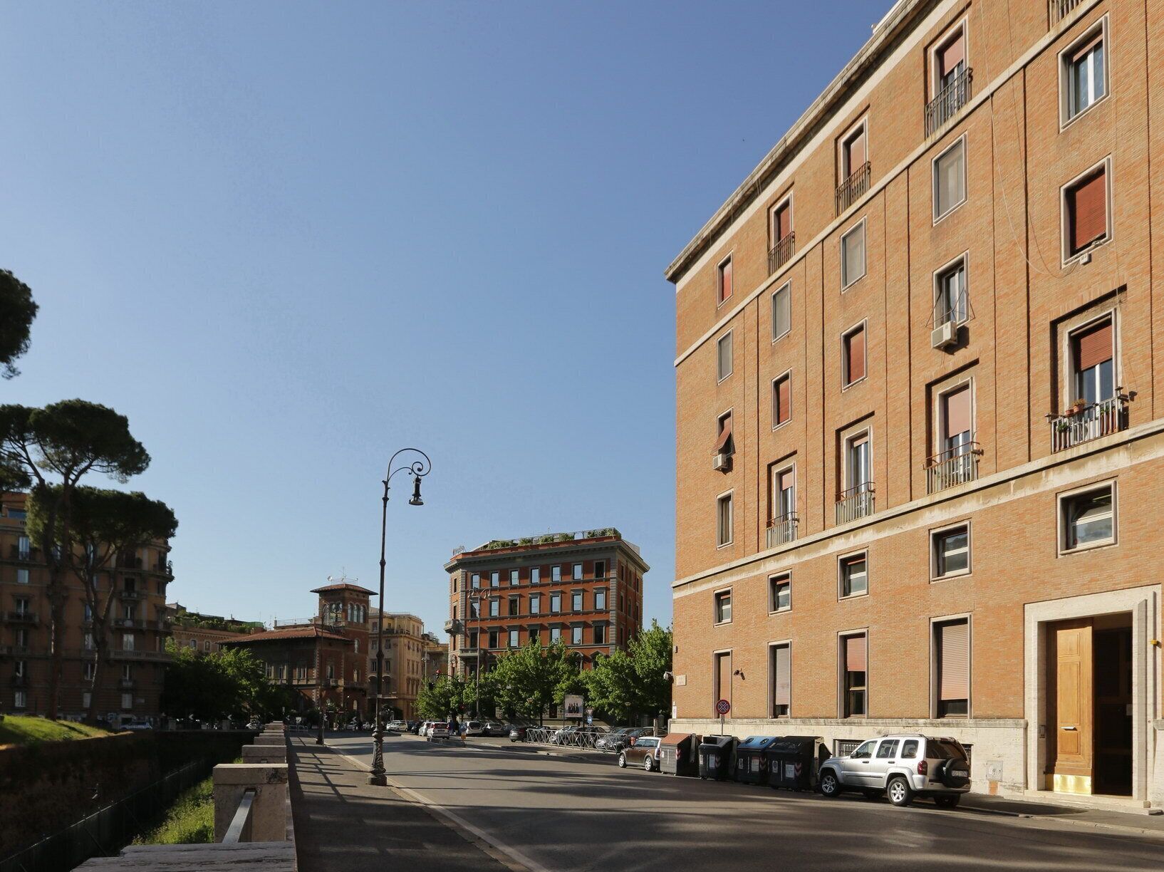 A street view with a row of brick buildings, some with balconies and windows, and a clear sky.