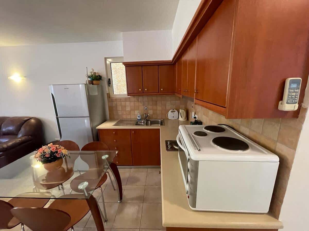 A compact kitchen with wooden cabinets, a white stove, and a dining area with a glass table and chairs.