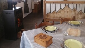 A cozy room with a wooden ceiling, a heart-shaped wooden decoration on the wall, a dining table set with plates and a glass, and a wood-burning stove. - Maisonnette 4/5 persons in Saint-Véran 2*. (Saint-Véran)