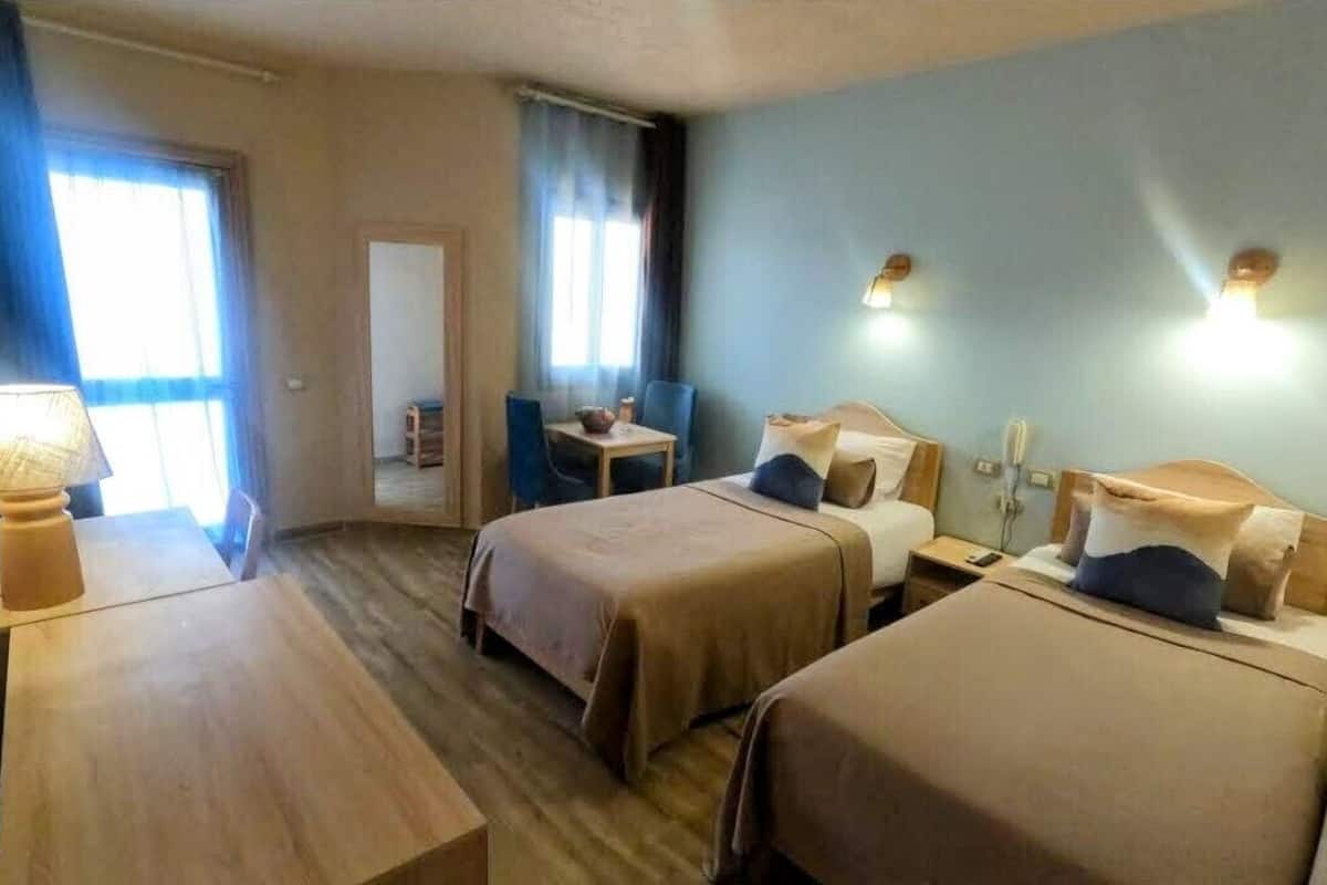 A hotel room with two beds, a small table, a chair, and a desk.