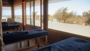 A massage room with two massage tables, a chair, and a view of a pool and trees. - Mangrove Bay Resort (El Quseir)