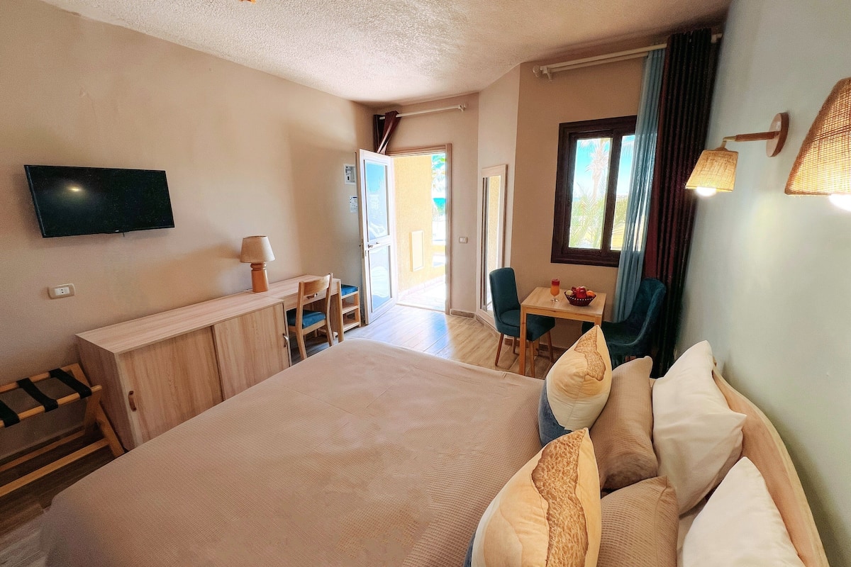 A hotel room with a large bed, a desk with a chair, a television, and a window with curtains.