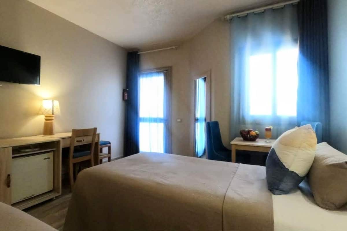 A hotel room with a bed, a desk, a chair, a television, and a window with curtains.