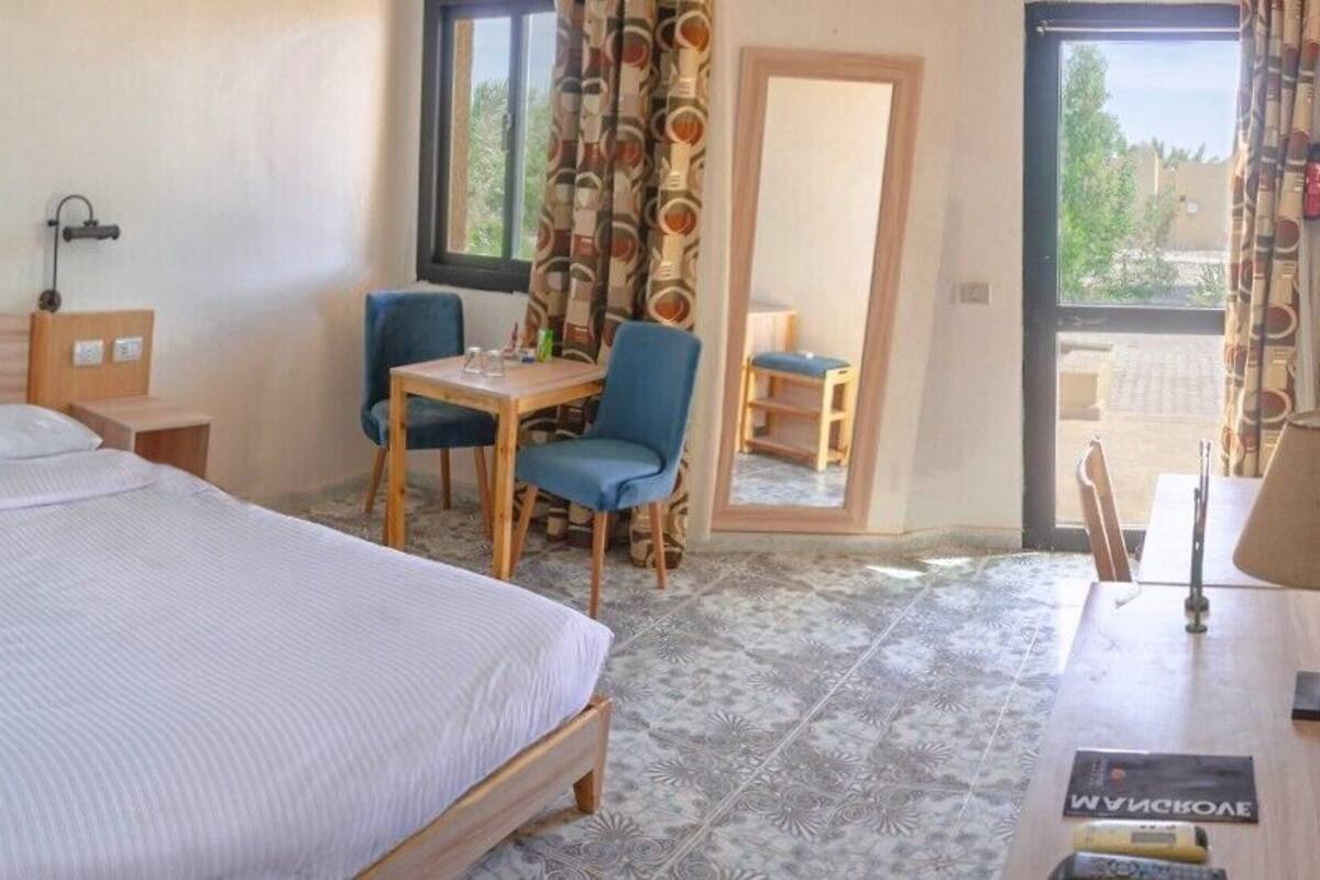 A hotel room with a bed, a desk, two chairs, a table, and a view through a window.