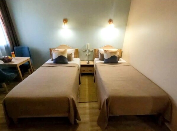 A hotel room with two single beds, a small table with a chair, and a desk with a chair. - Mangrove Bay Resort (El Quseir)