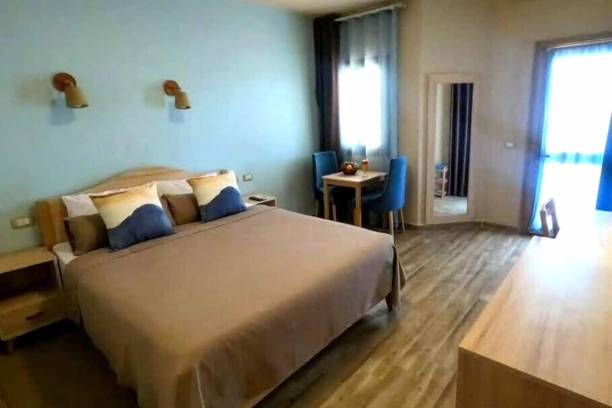 A hotel room with a large bed, a small table with chairs, and a view of the outdoors.