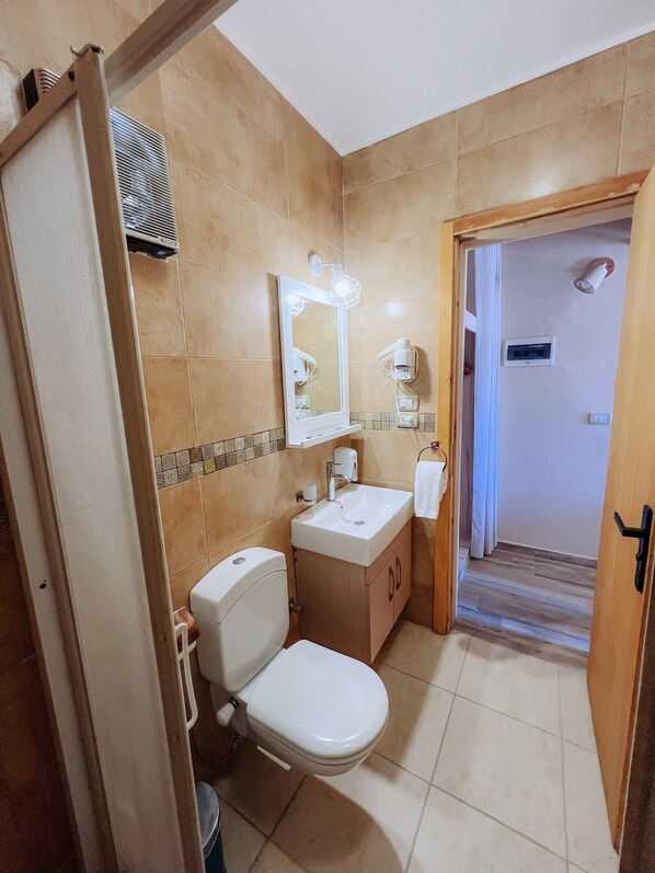 A bathroom with a toilet, sink, mirror, and shower area.
