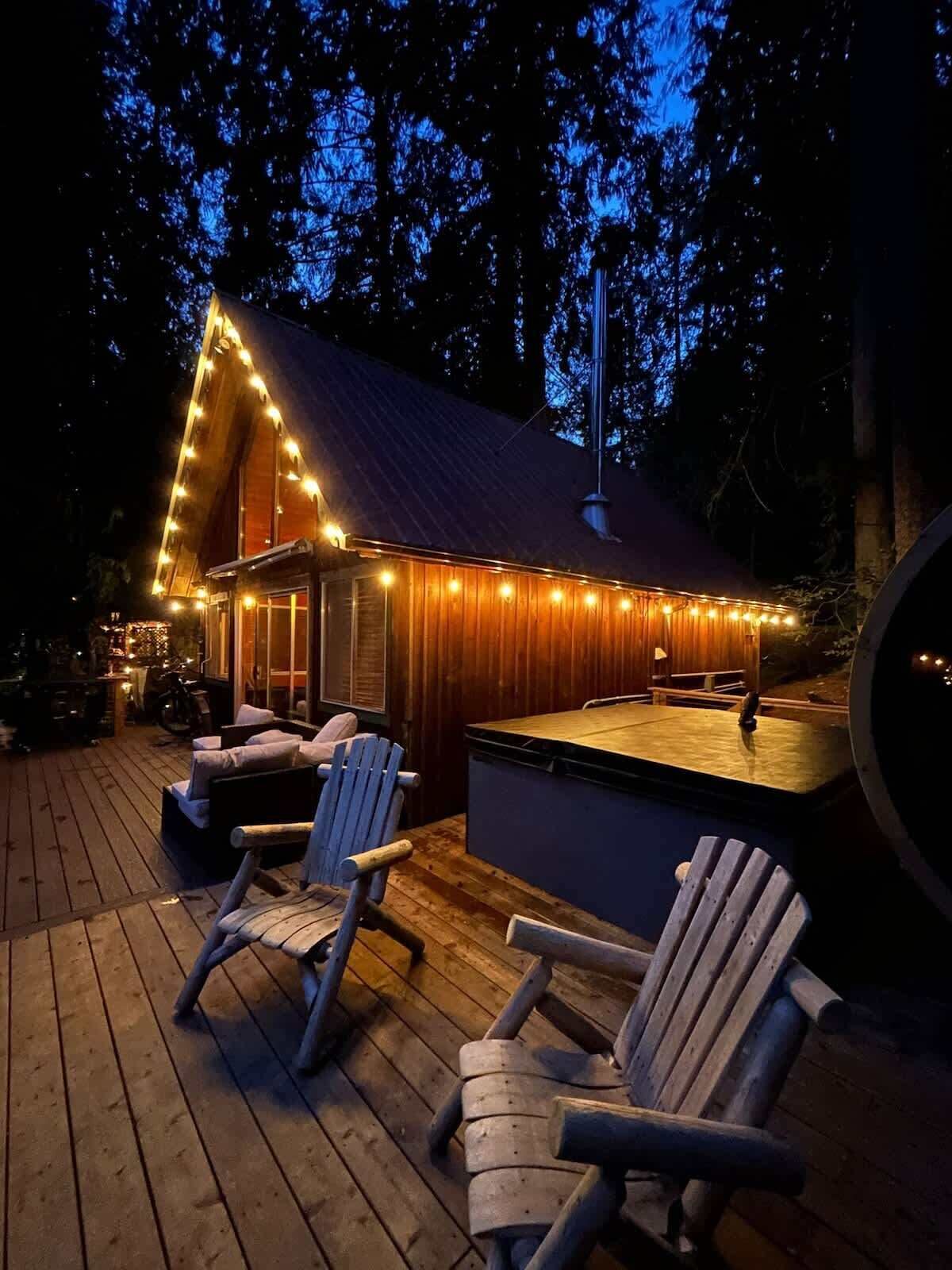 Una terraza de madera con sillas Adirondack, un jacuzzi y luces colgantes.