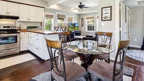 Een moderne keuken met witte kastjes, een centraal eiland en een eethoek met een glazen tafel en metalen stoelen.
