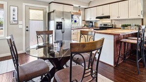 Een moderne keuken met een centraal eiland, roestvrijstalen apparatuur en een eethoek met een glazen tafel en metalen stoelen.