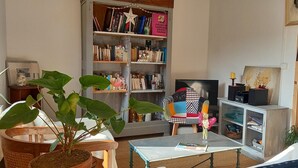 A cozy living room with a bookshelf, a television, and a dining area. - Charming, quiet town house with small garden  (Crest)