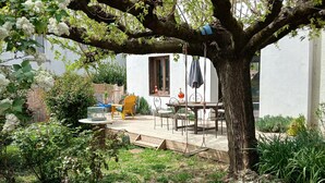 A tree with a patio area featuring outdoor furniture and a white building in the background. - Charming, quiet town house with small garden  (Crest)