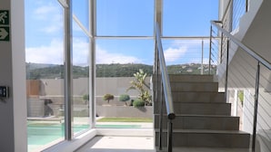 Ein modernes Interieur mit einer Treppe zu einem Außenbereich, großen Fenstern und Blick auf einen Pool.