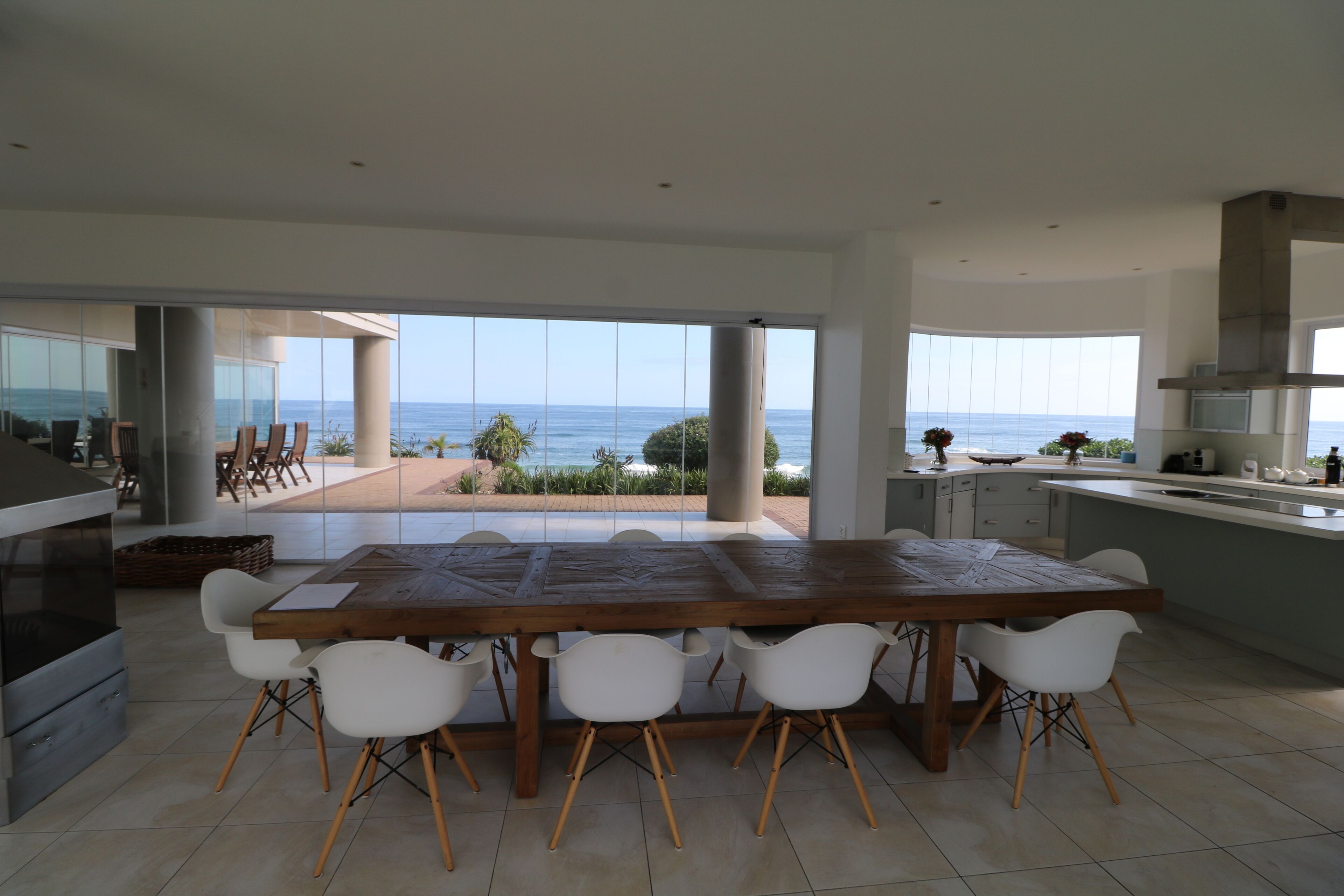 A modern kitchen with a large island, white chairs, and a view of the ocean.