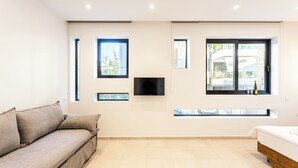 Ein modernes Wohnzimmer mit Sofa, Bett, Fernseher und großen Fenstern.