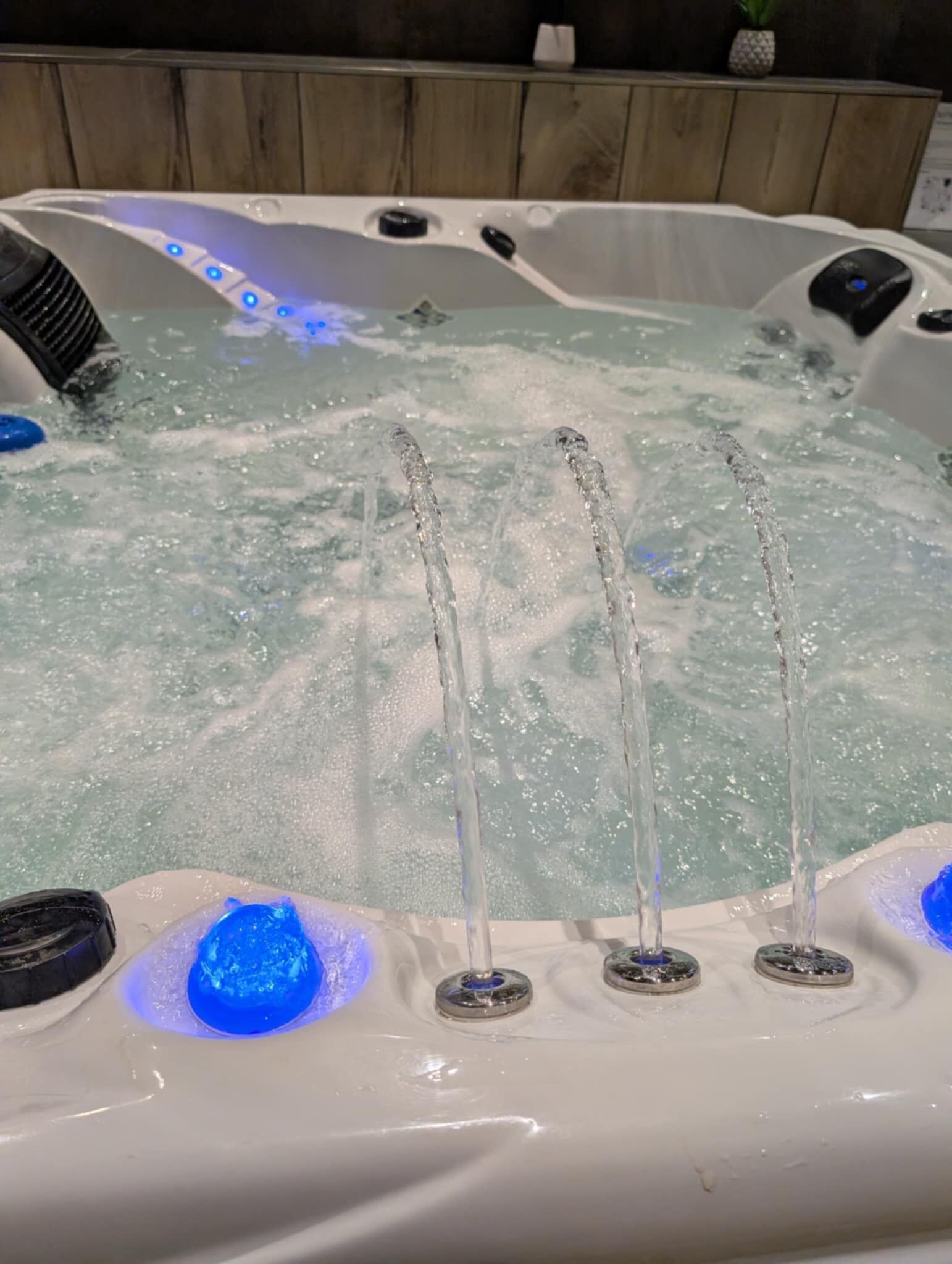 A hot tub with three jets of water, a blue light, and a wooden backdrop.