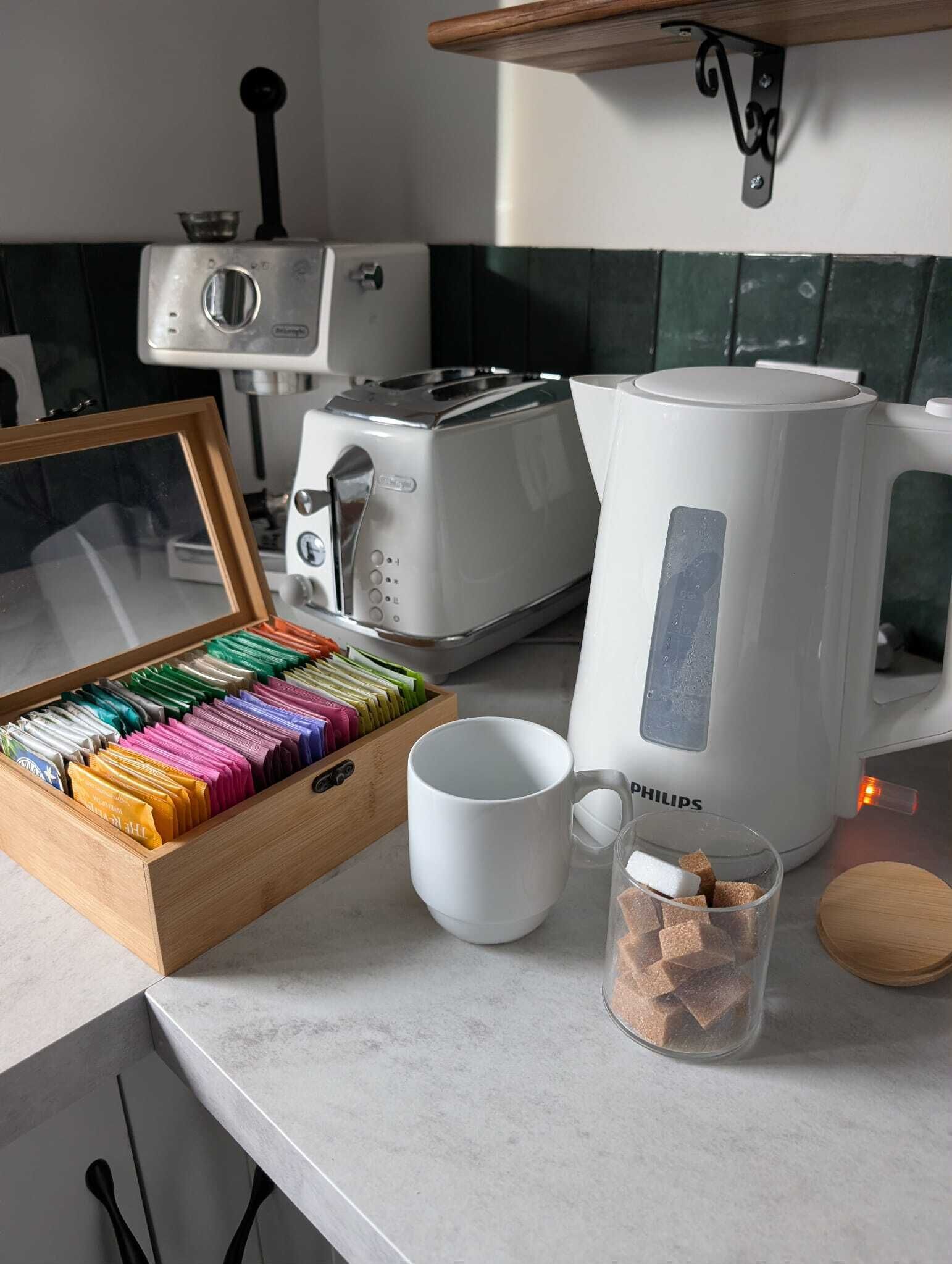 A kitchen with a toaster, a coffee maker, a mug, and a drawer of colorful utensils.