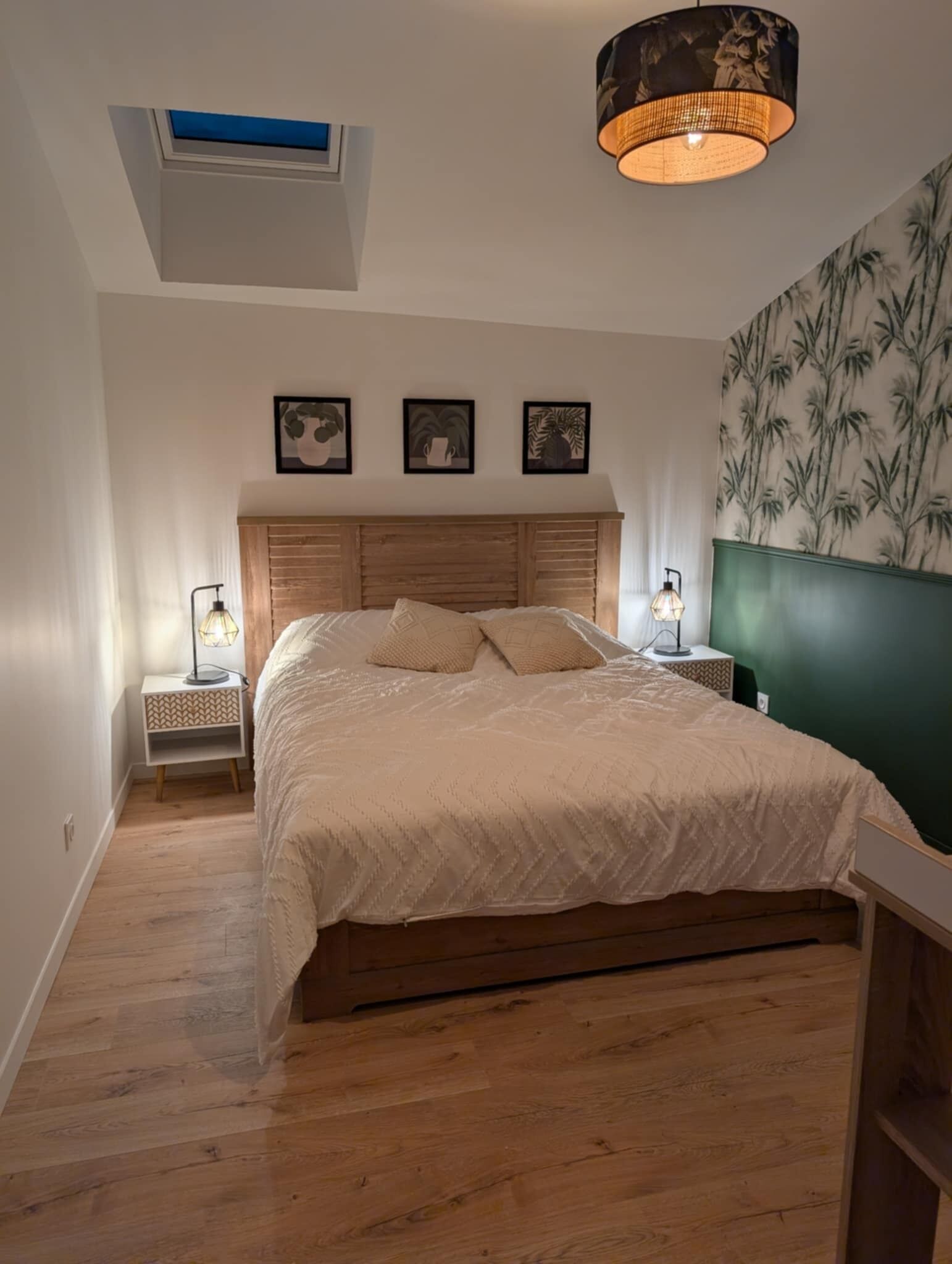 Une chambre avec un lit en bois, un puits de lumière et un mur décoré d’un motif en bambou.