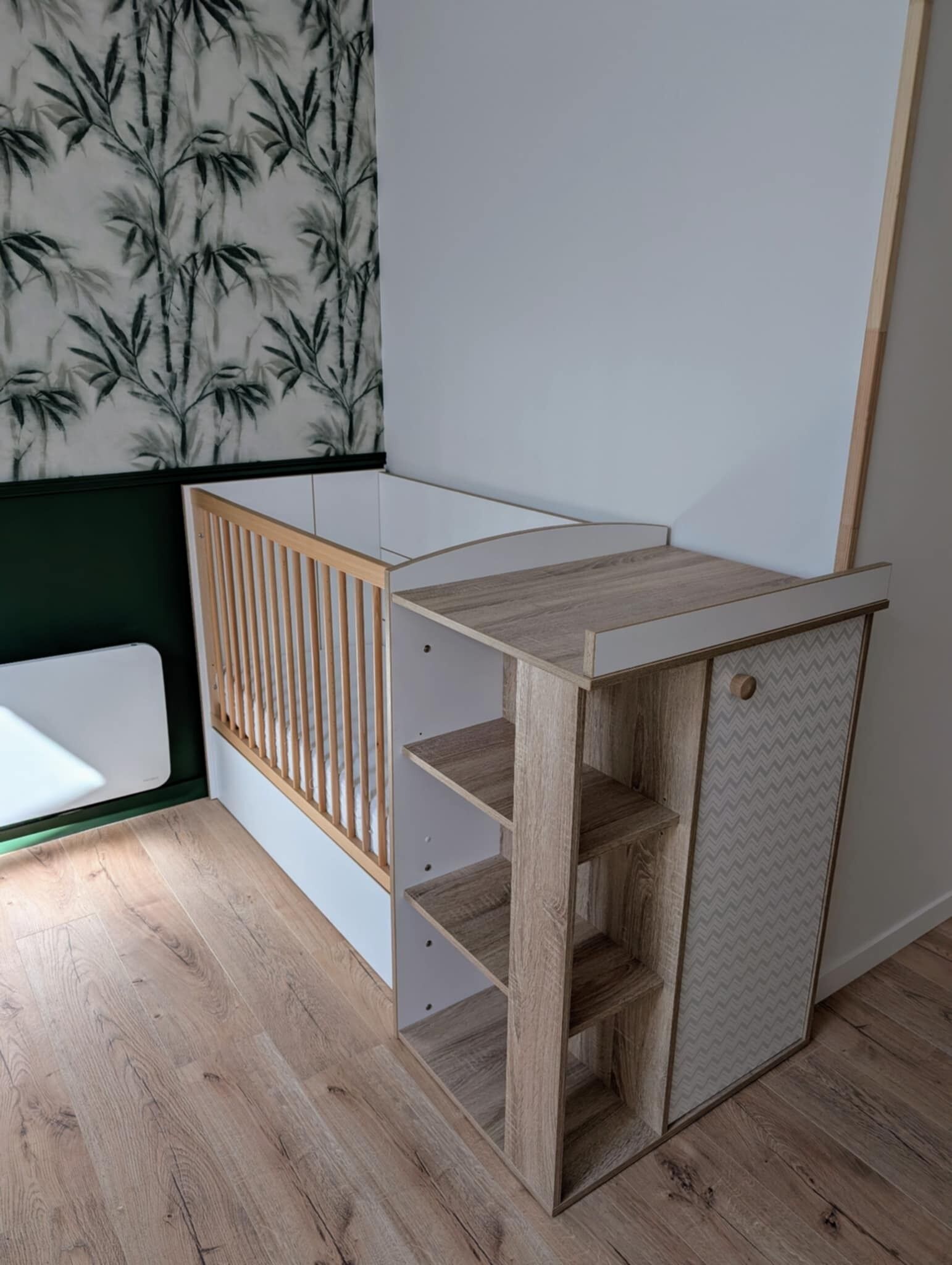 A corner room with a wooden crib, a built-in desk with shelves, and a patterned wall.