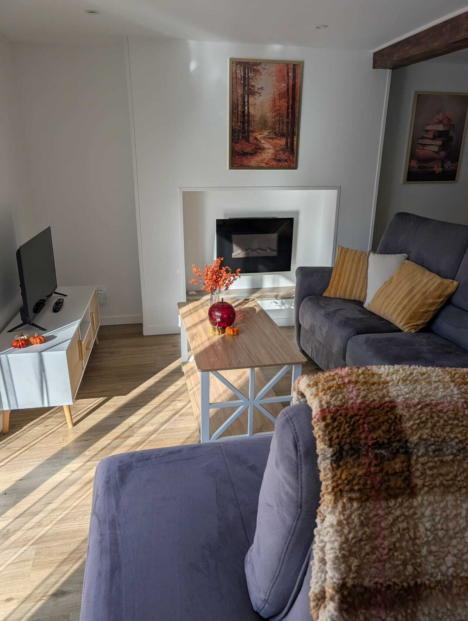 En moderne stue med pejs, sofa, sofabord med dekorative genstande og fjernsyn på et sofabord.
