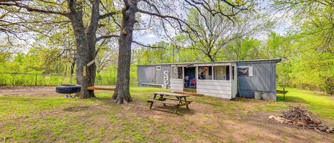 A rustic cabin with a wooden deck, a picnic table, and a tire swing.