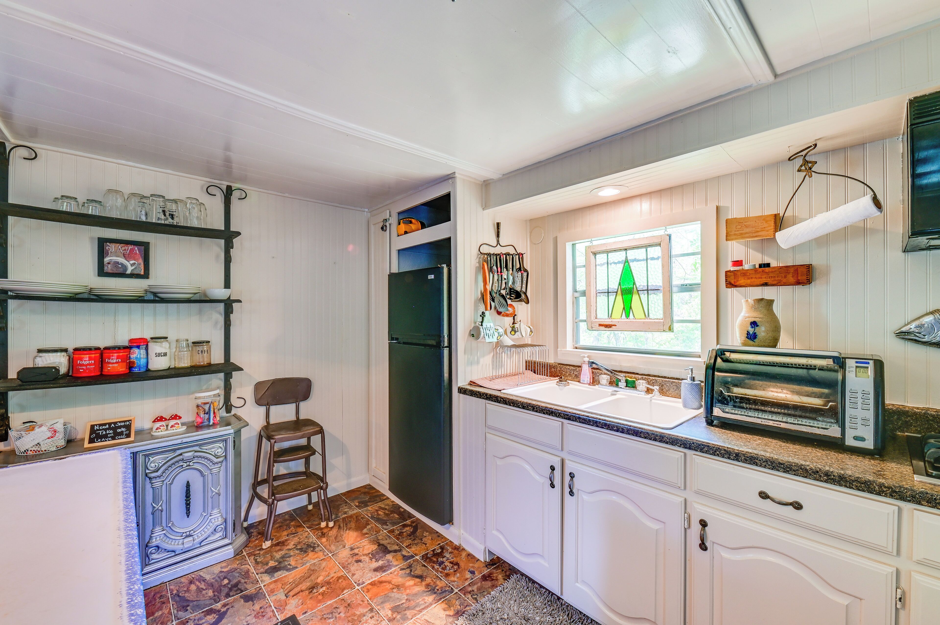 A kitchen with white cabinets, a black refrigerator, a sink, and a toaster.