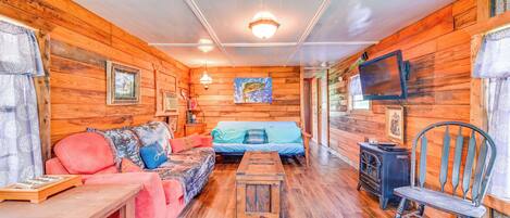 Ein gemütliches Blockhauszimmer mit Holzwänden, einer Couch, einem Bett, einem Holztisch, einem Stuhl und einem Fernseher.