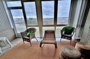 A room with large windows, wicker furniture, and a view of a field.