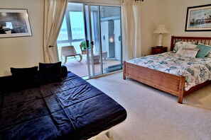 Ein Schlafzimmer mit einem Bett, einem Sessel, einer Lampe und Blick durch eine Glastür.