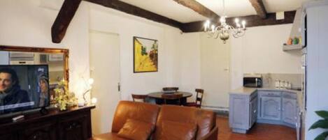 A living room with a brown leather sofa, a television, and a dining area with a table and chairs.