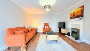 Een moderne woonkamer met een bank, salontafel, televisie, open haard en kunstwerken.