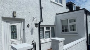 Een wit huis met twee verdiepingen, een klein voortuintje, een zwart metalen hek en een heldere lucht.