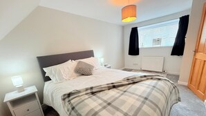 Een slaapkamer met een bed, nachtkastjes, een lamp, een raam met gordijnen en een radiator.