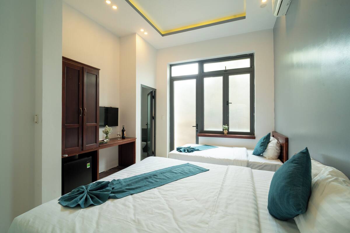 A hotel room with two beds, a desk with a computer, a wardrobe, and a large window.