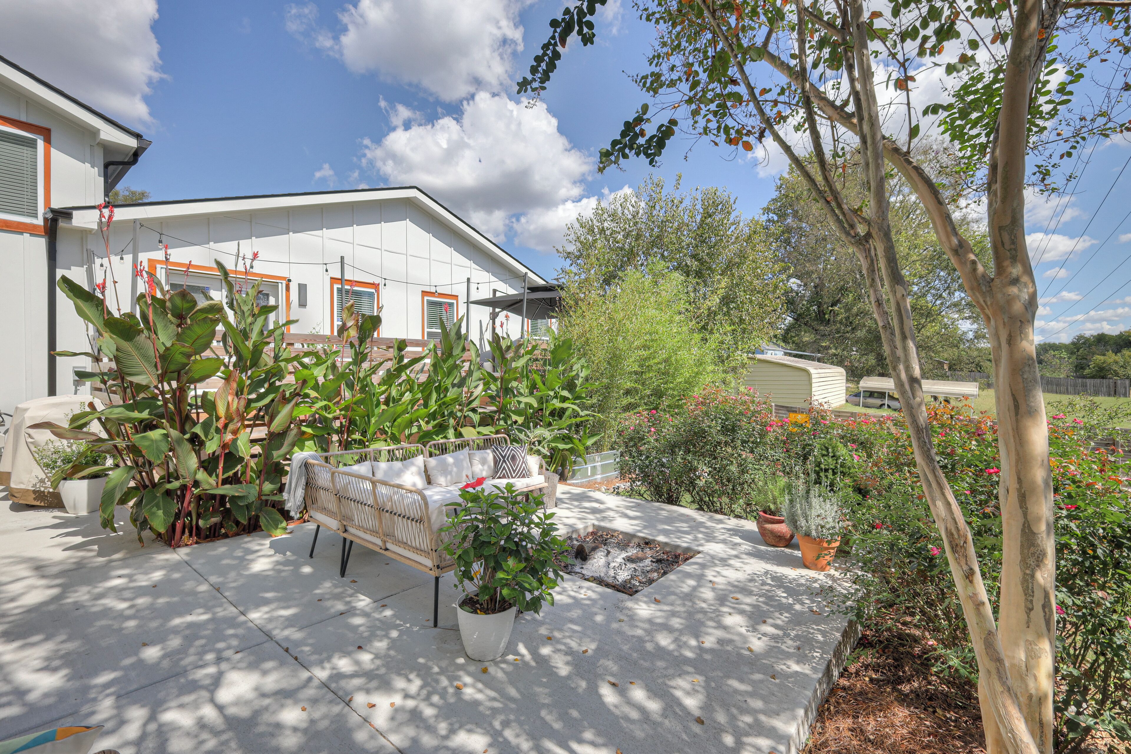 Ein modernes Haus mit überdachter Terrasse, Gartenmöbeln und diversen Pflanzen.