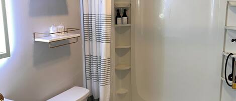 Une salle de bain moderne équipée de toilettes, d’une douche et d’étagères où sont rangés les produits de toilette.